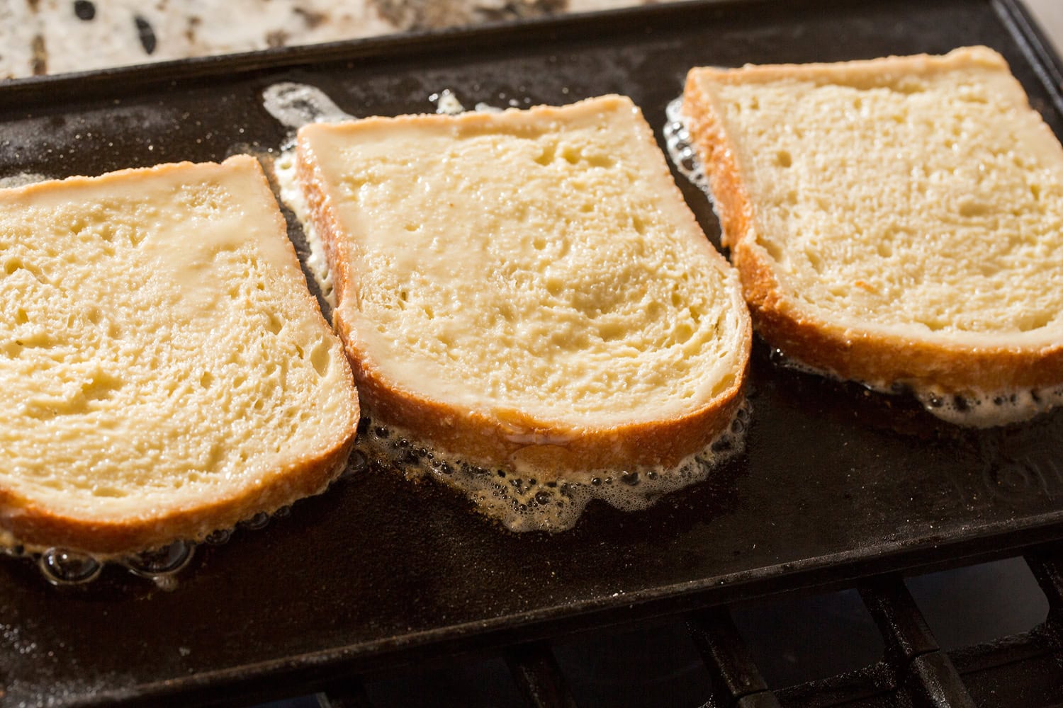 Buttermilk French Toast Raw french toast cooking on first side on griddle with butter.