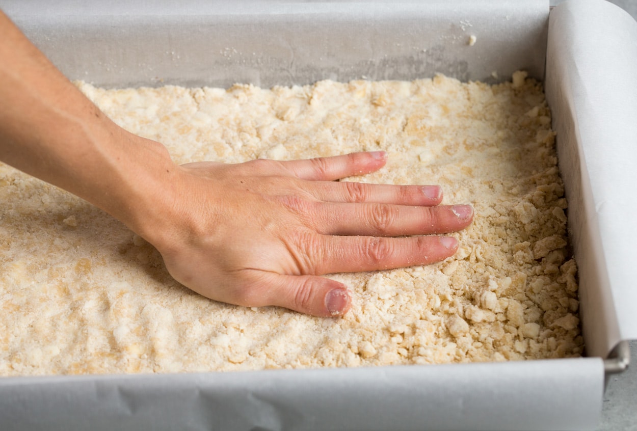 adding first layer of crumbs to pan for blueberry bars