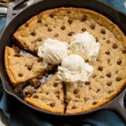 Skillet chocolate chip cookie with two wedges cut and three vanilla ice cream scoops on top.