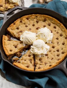 Skillet chocolate chip cookie with two wedges cut and three vanilla ice cream scoops on top.