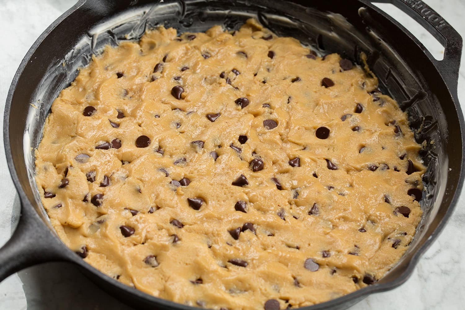 Skillet Chocolate Chip Cookie Chocolate chip cookie batter in a cast iron skillet shown before baking.