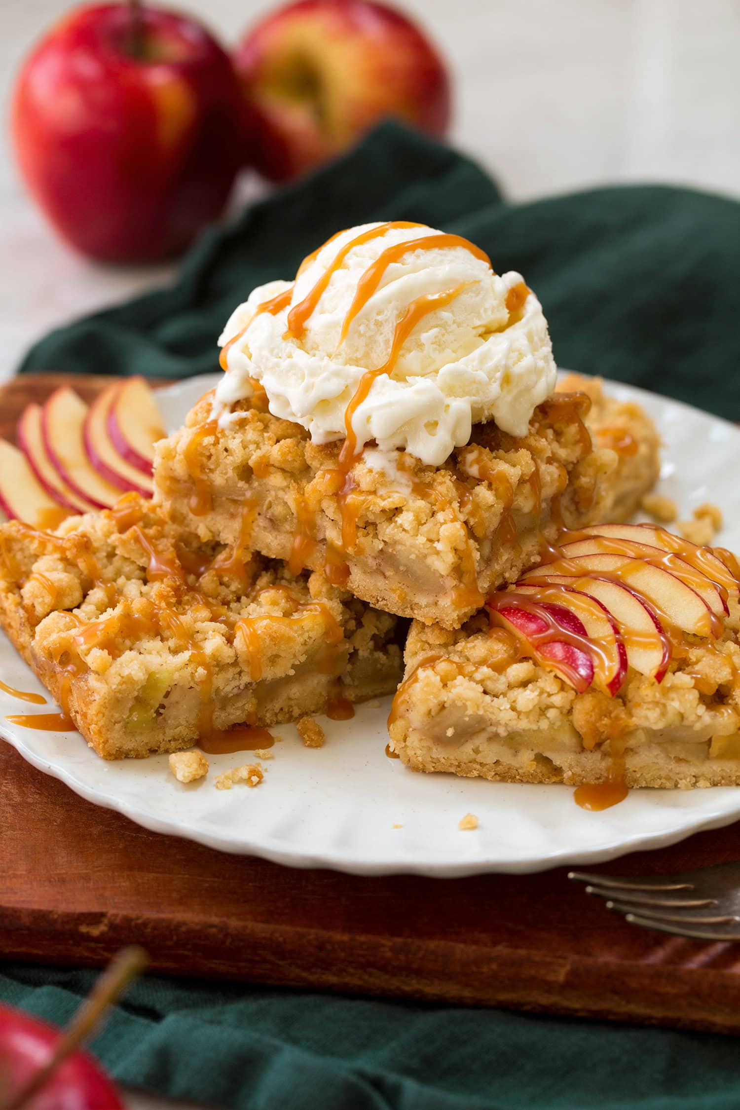 Apple Pie Bars Three apple pie crumb bars stacked on a plate with a scoop of vanilla ice cream on top and drizzled with caramel sauce.