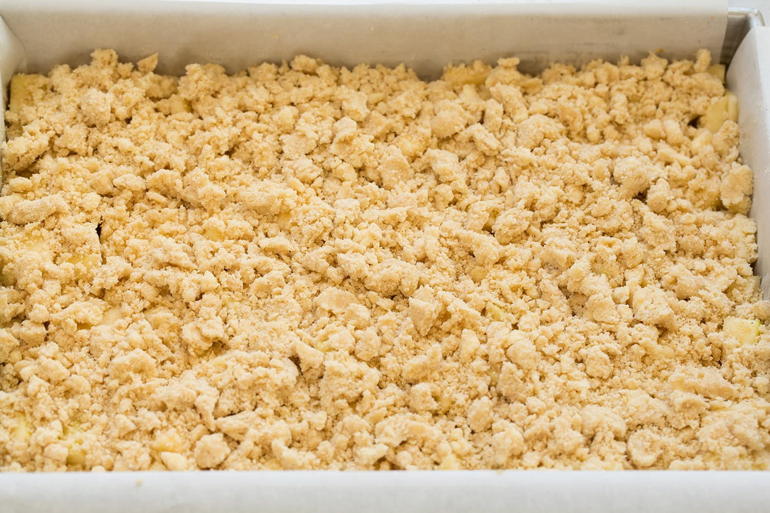 Apple Pie Bars Crumble mixture sprinkled over top of apple layer in baking dish.