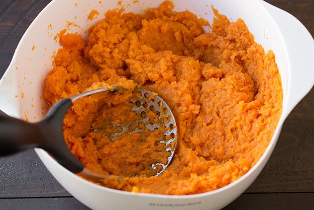 Browned Butter Sweet Potato Casserole Mashing sweet potatoes in a mixing bowl.