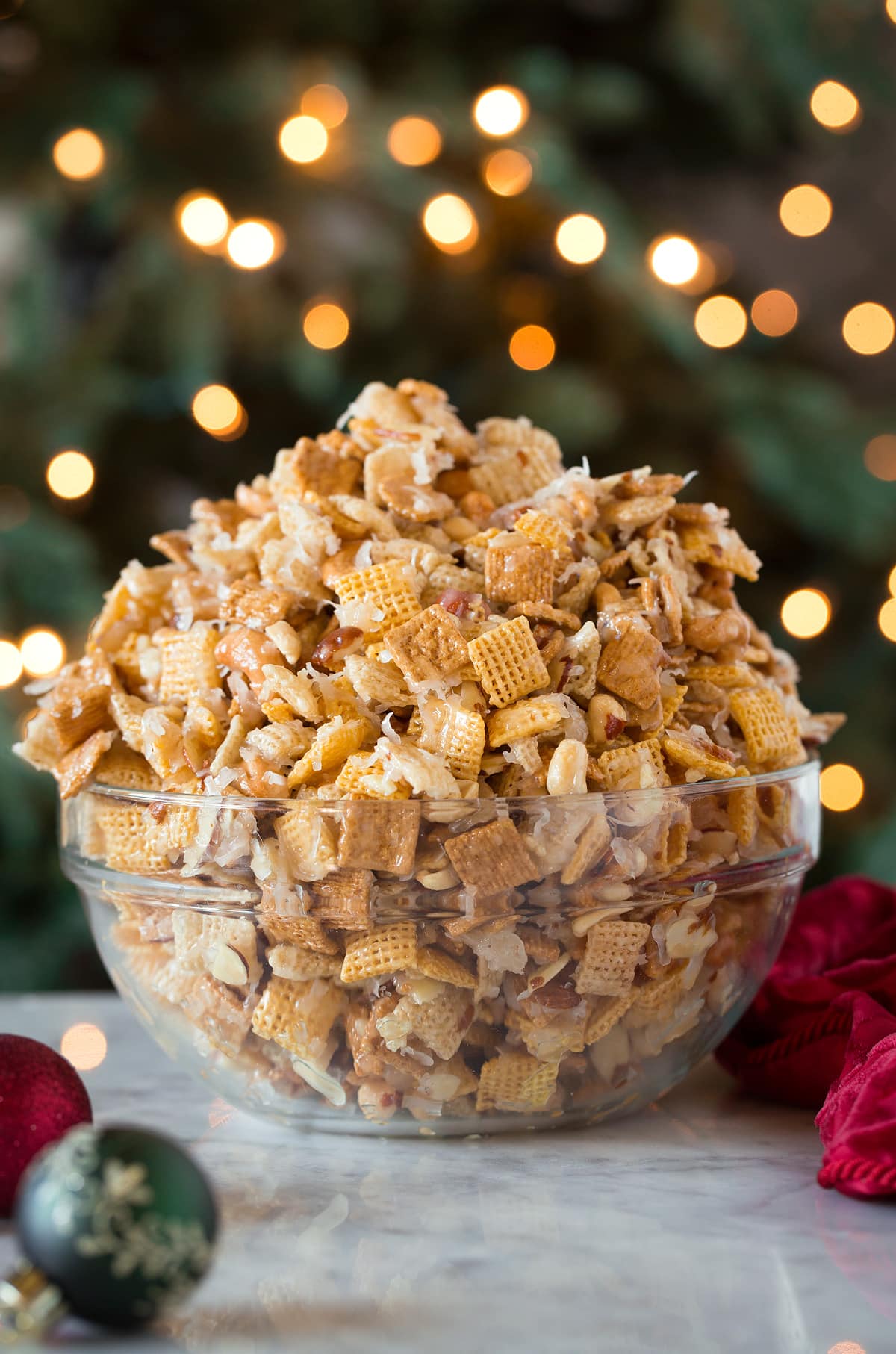 Sweet Holiday Chex Mix Sweet Chex Mix in front of a Christmas tree in a glass bowl.