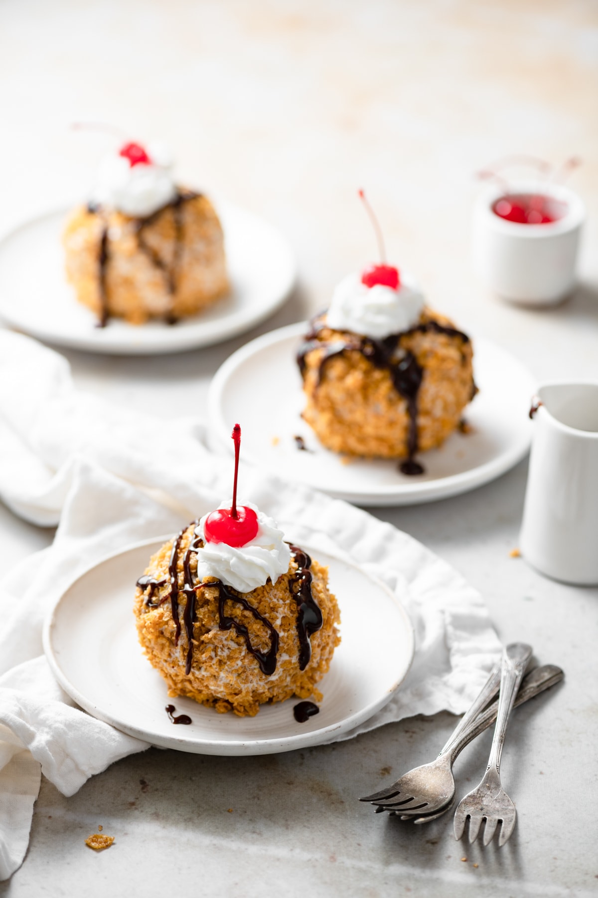 BEST EVER Easy Fried Ice Cream! Three individual servings of fried ice cream coated in cinnamon cornflake topping, drizzled with chocolate sauce and garnished with a cherry.