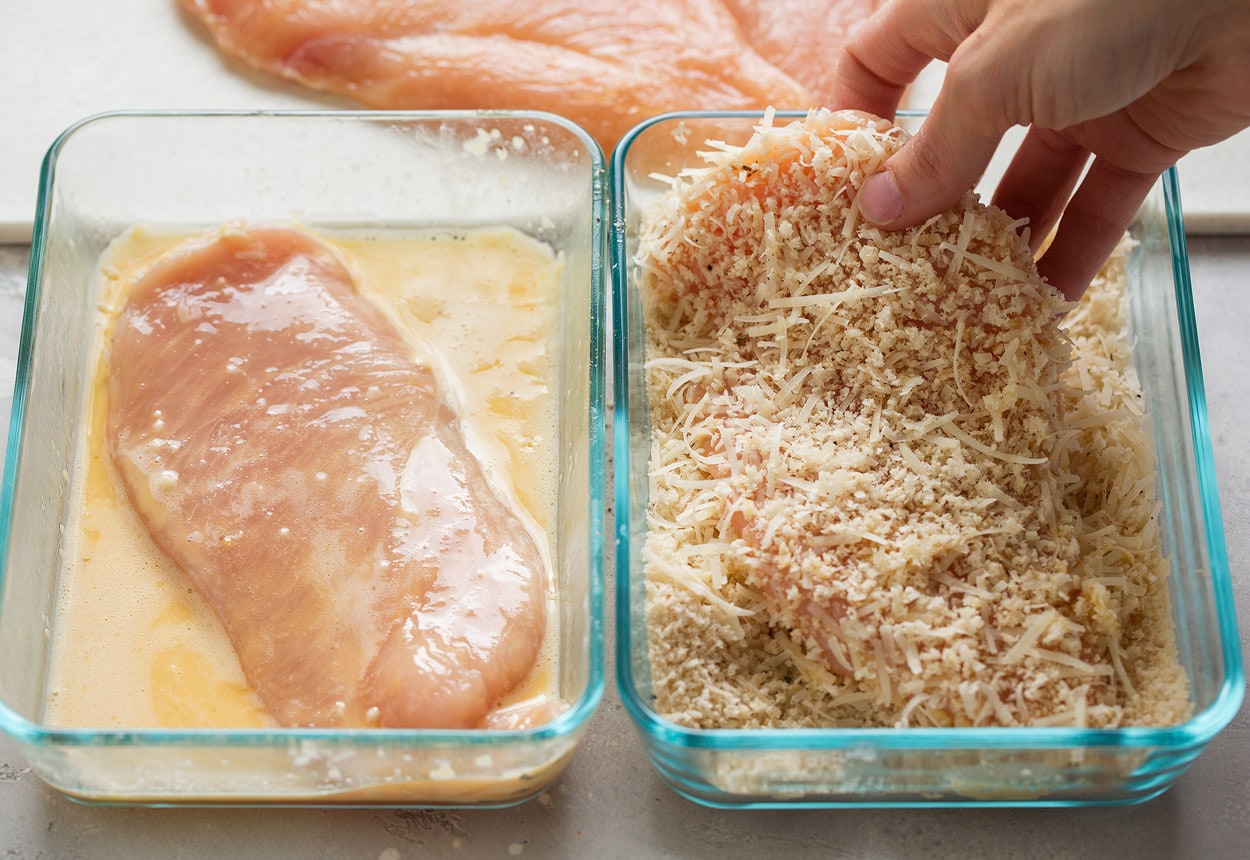 BEST Chicken Parmesan recipe! Showing how to make chicken parmesan. Dredging chicken cutlets in egg in shallow glass dish on left side then Panko parmesan mixture in shallow glass dish on right side.