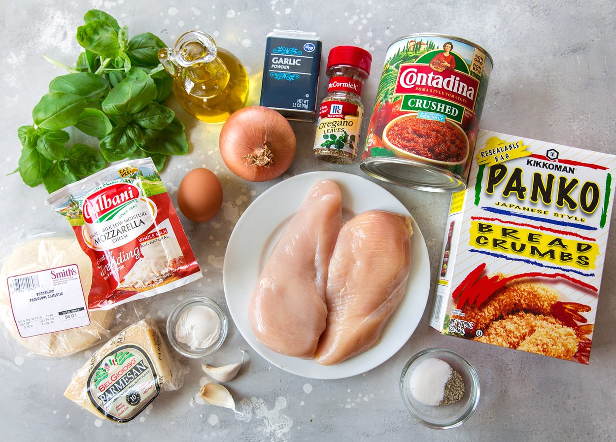 BEST Chicken Parmesan recipe! Ingredients needed for chicken parmesan shown here including panko, chicken breasts, crushed tomatoes, oregano, dried and fresh garlic, onion, egg, olive oil, basil, mozzarella, provolone, parmesan, and flour.