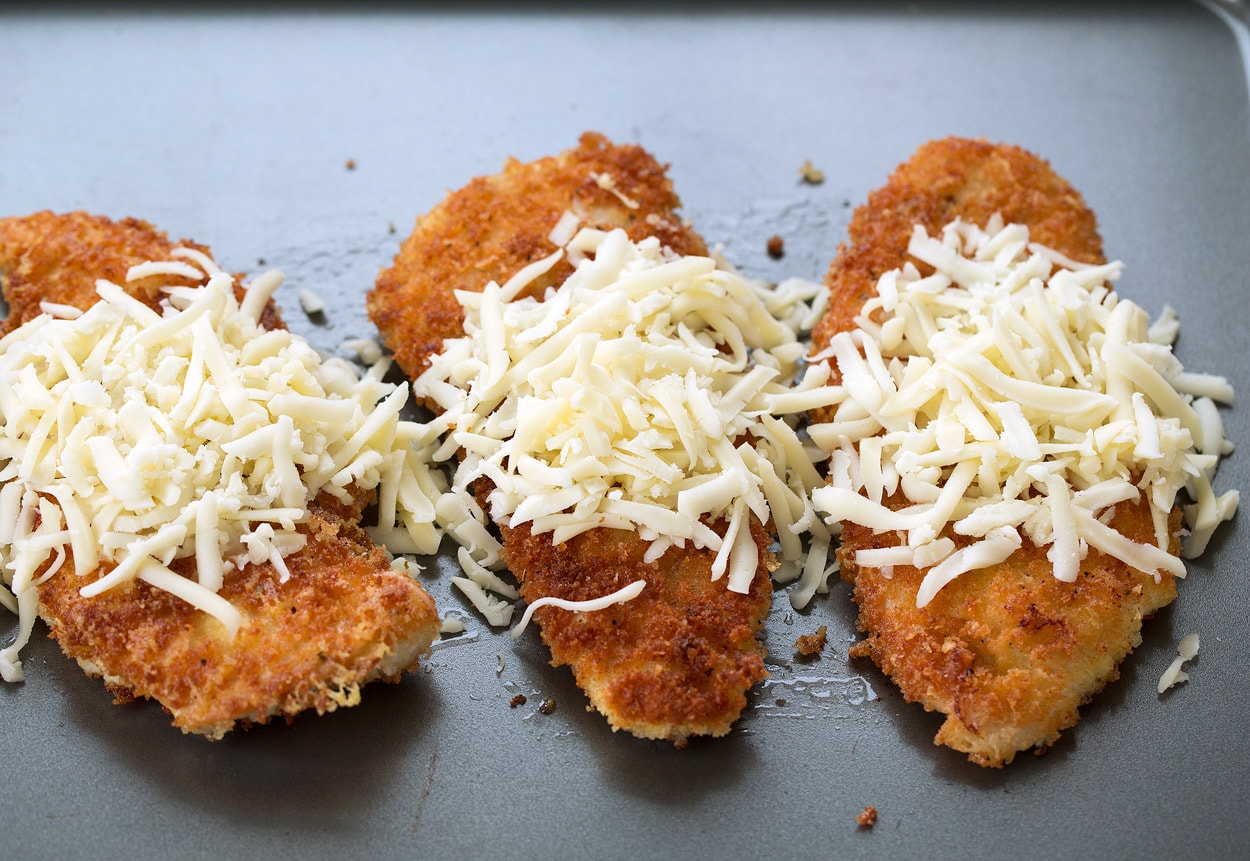 BEST Chicken Parmesan recipe! Placing browned chicken cutlets on baking sheet then covering with shredded cheeses.