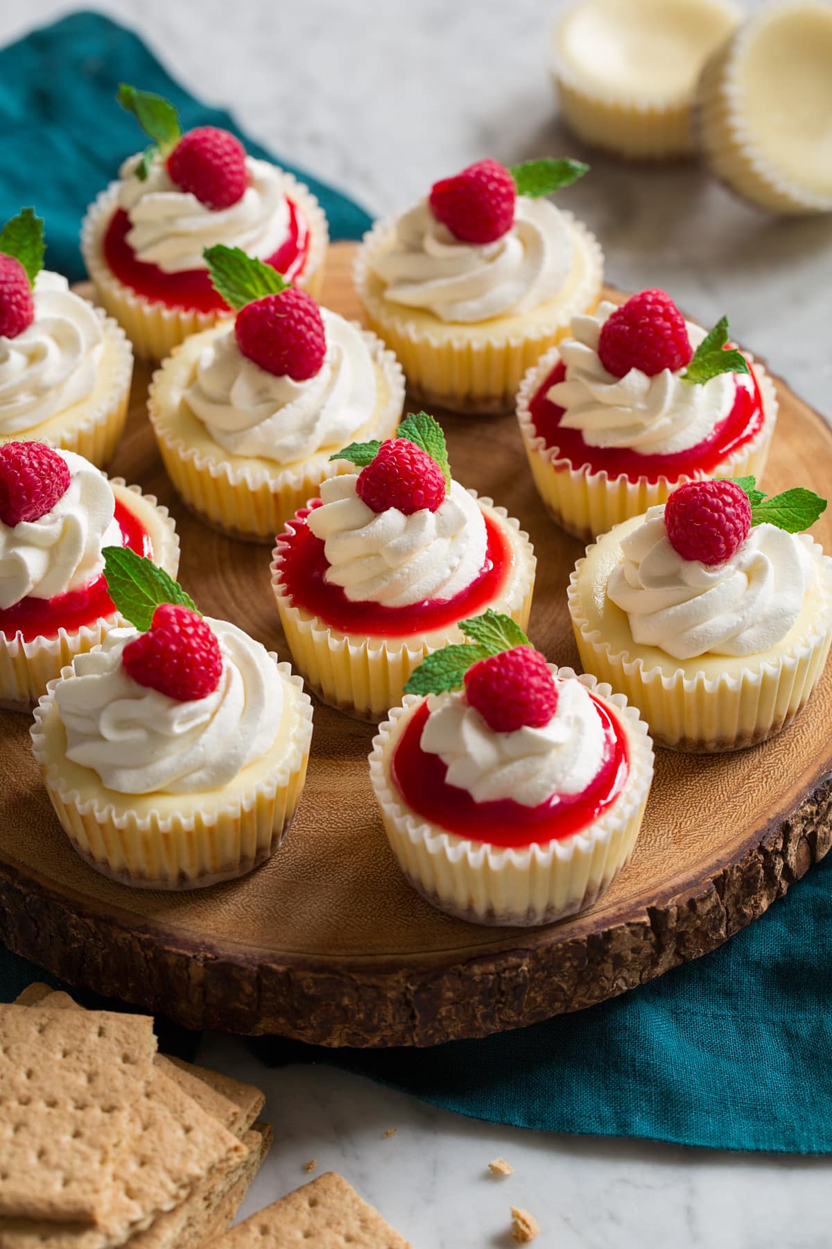 Mini Cheesecakes Mini cheesecakes topped with raspberry sauce and whipped cream and mint. Shown sitting on a wooden serving stand.