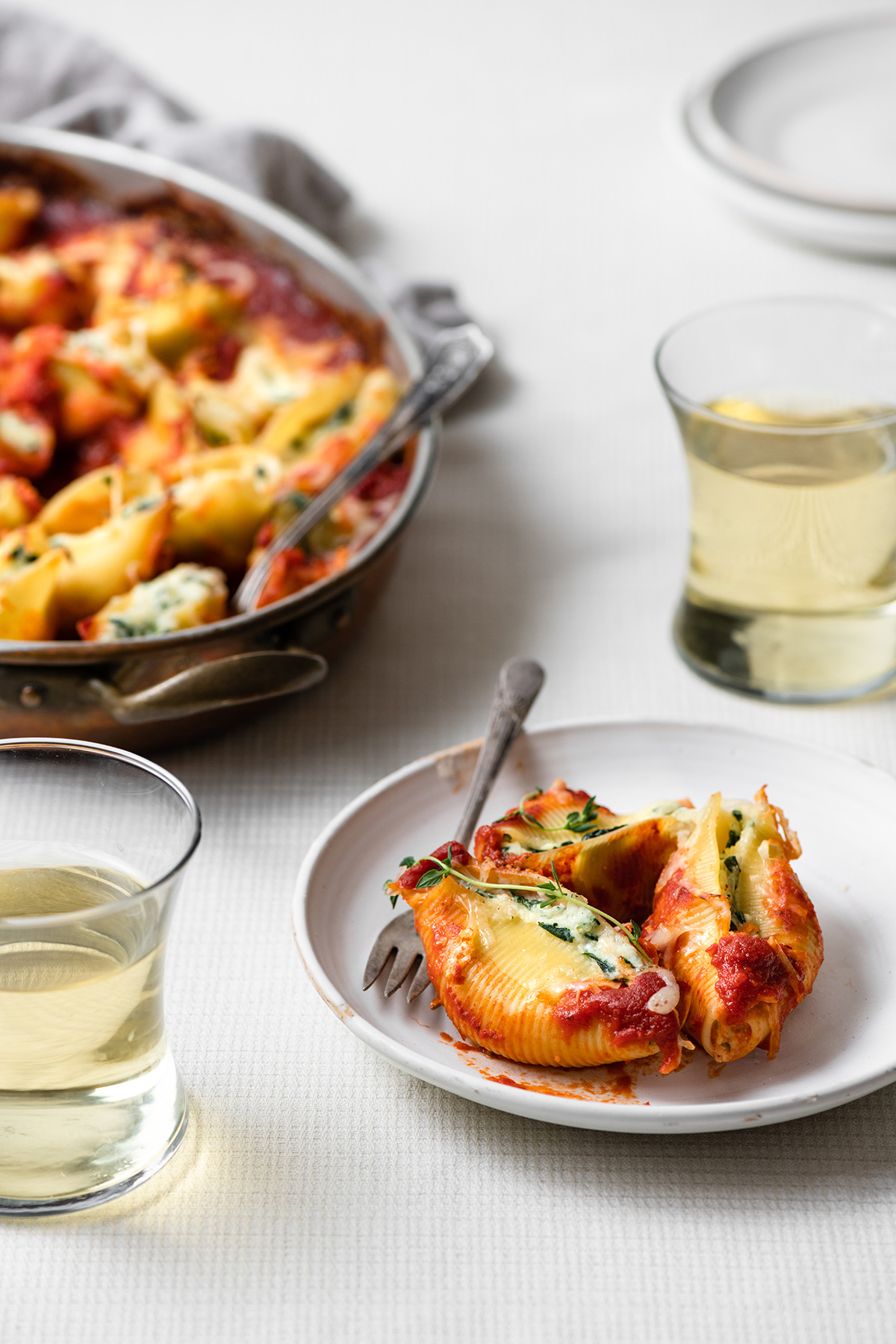 Spinach and Cheese Stuffed Shells Stuffed shells on a white serving plate with the baking dish of stuffed shells in the background.
