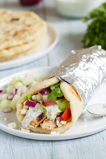 Gyros with Juicy Greek Chicken, tangy Tzatziki sauce and soft and fluffy homemade Greek pita flatbreads. These Gyros are insanely delicious and can be filled with your favorite veggies and salad. #Gyros #Chicken #Greekfood #Tzatziki homemade Gyros with Greek Chicken & Tzatziki Sauce on a plate