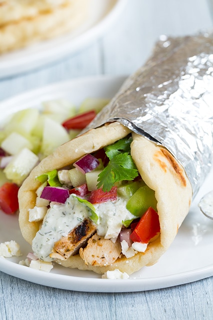 Gyros with Juicy Greek Chicken, tangy Tzatziki sauce and soft and fluffy homemade Greek pita flatbreads. These Gyros are insanely delicious and can be filled with your favorite veggies and salad. #Gyros #Chicken #Greekfood #Tzatziki chicken Gryos with Tzatziki Sauce on a white plate