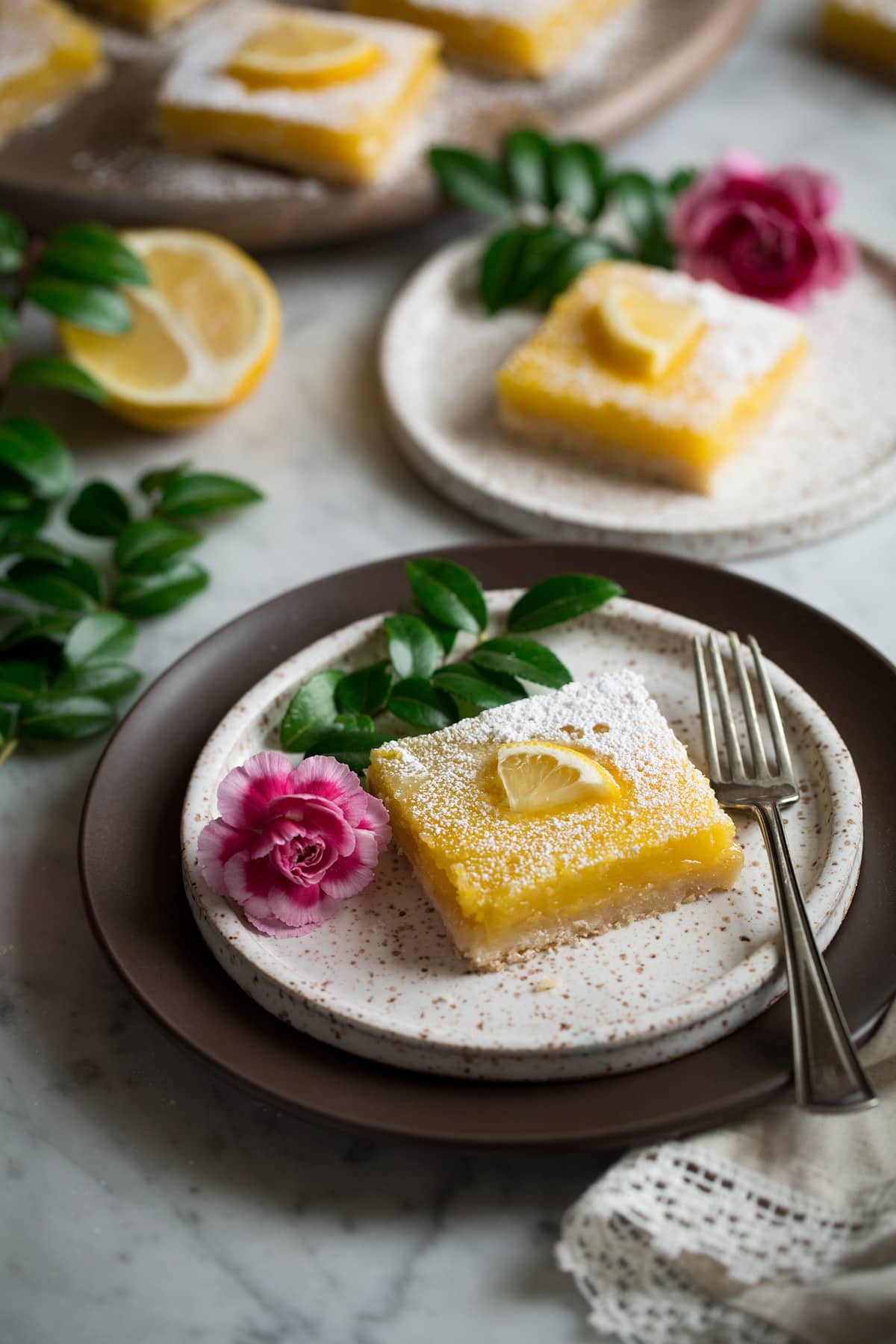 Lemon Bars Recipe Lemon Bars or two dessert plates decorated with flowers and greens.