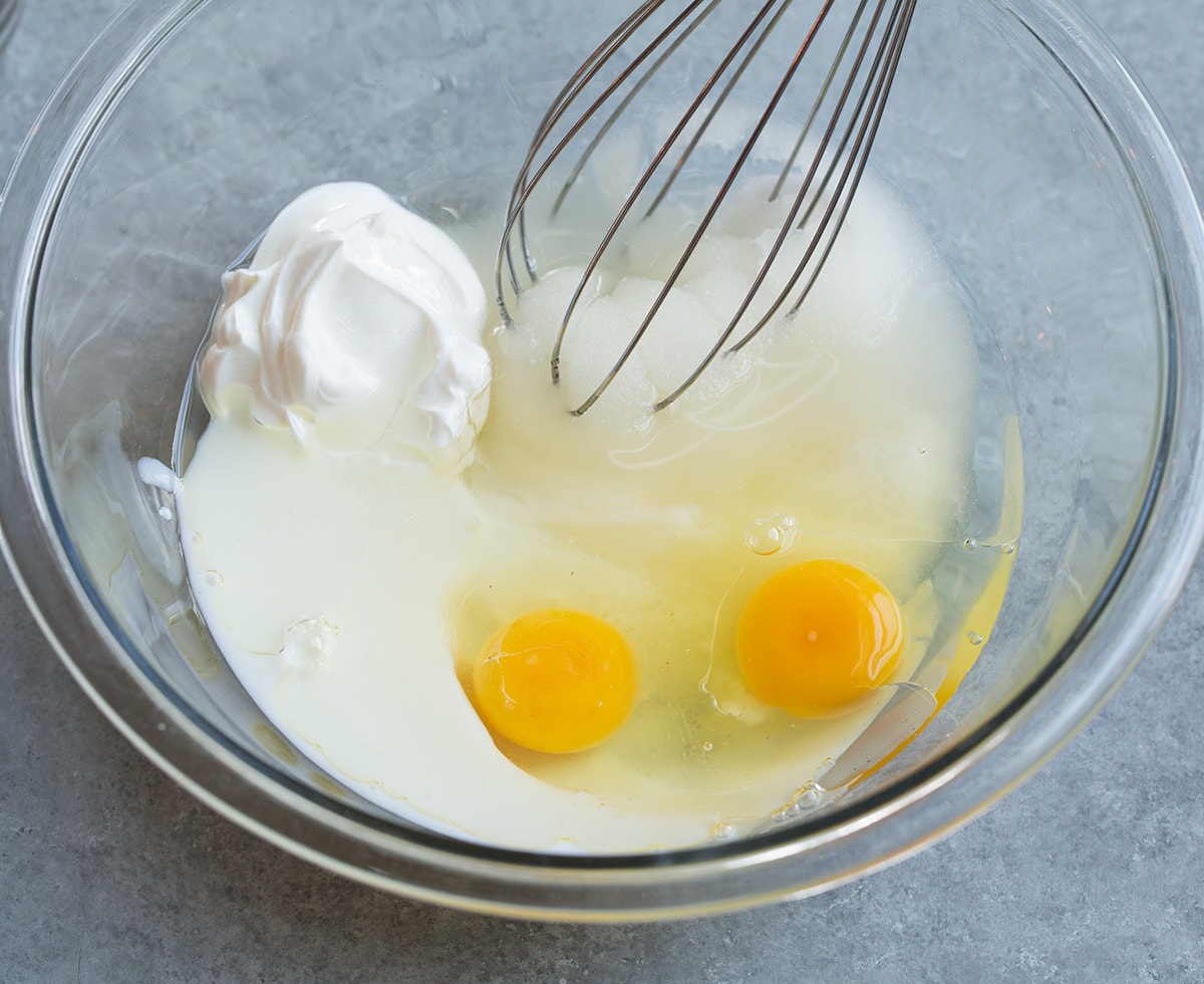 Mixing eggs, sour cream, buttermilk, sugar and oil in a mixing bowl for blueberry muffins.