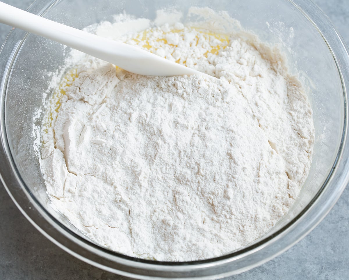 Folding flour mixture into blueberry muffin batter in mixing bowl.