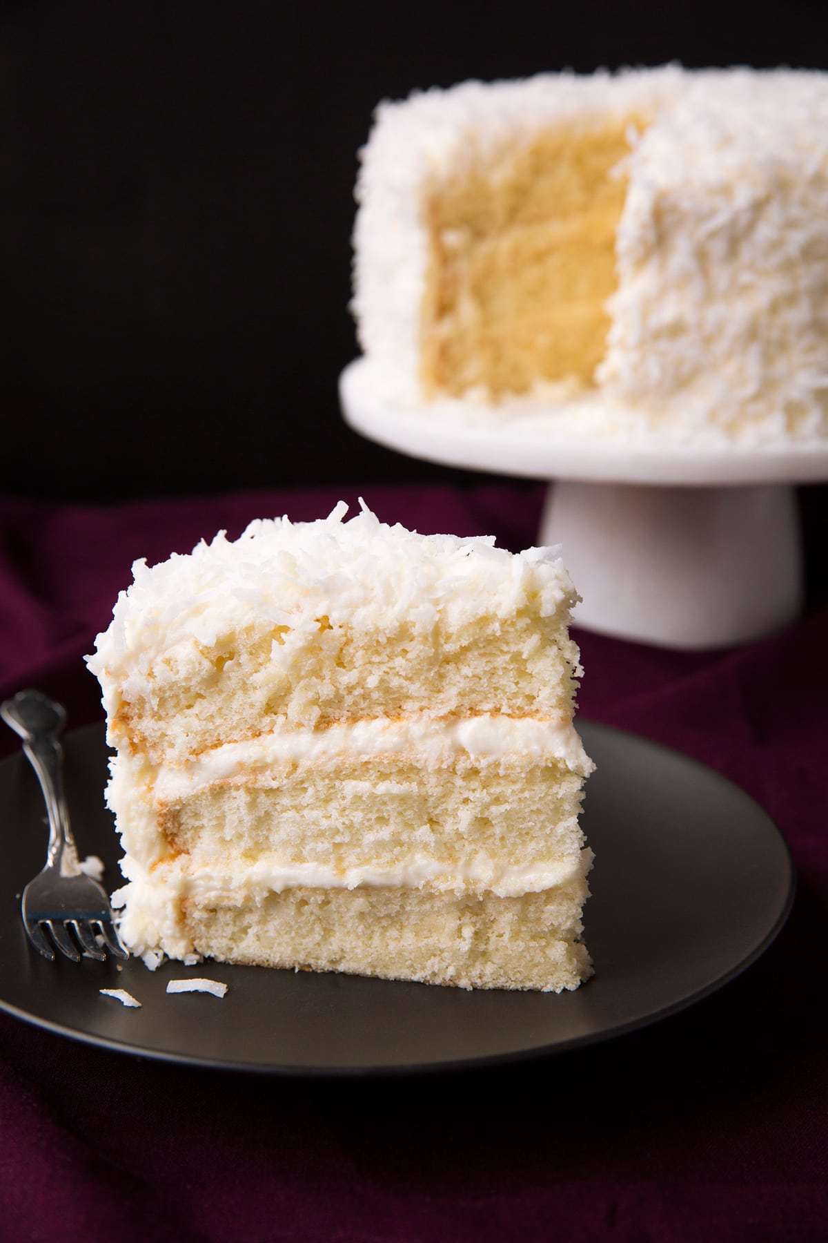 Best Ever Coconut Cake! Single slice of easy coconut cake with a remainder of cake in the background.