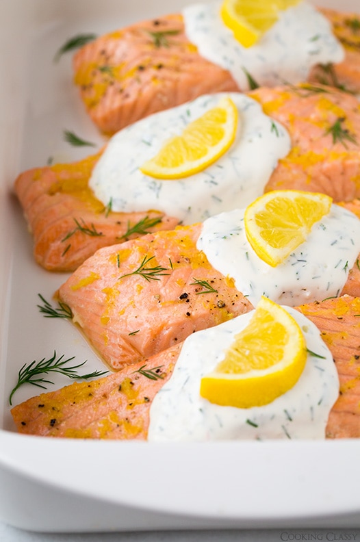 close up of lemon salmon garnished with yogurt sauce and lemon slices in baking dish