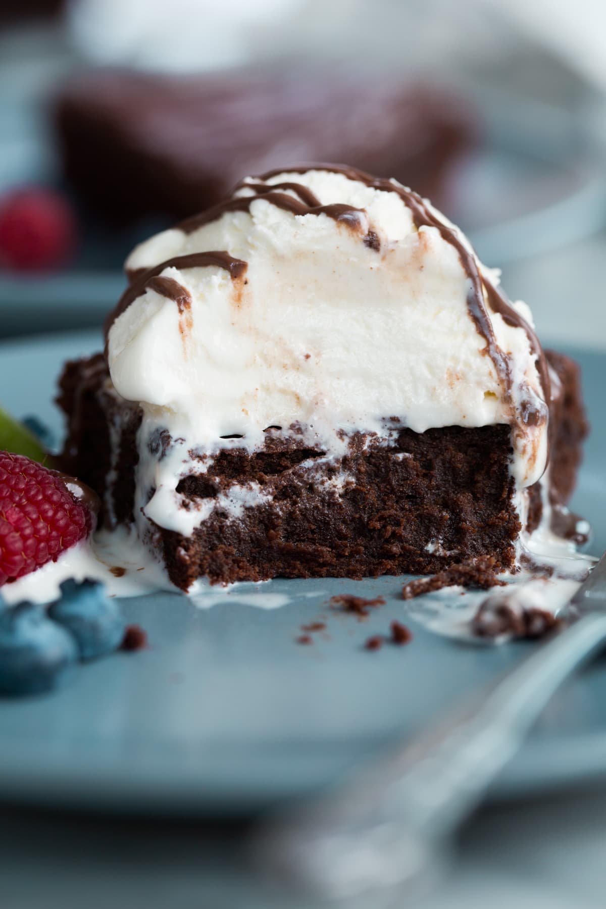 The BEST Flourless Chocolate Cake! Flourless chocolate cake with several bites eaten to showing. It's topped ice cream and chocolate sauce.