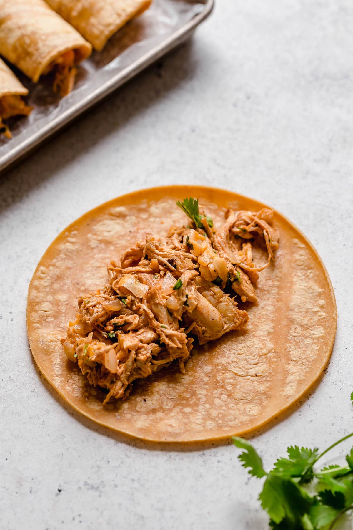 Baked Chicken Taquitos Showing how to make taquitos, piling chicken filling into center of corn tortilla.