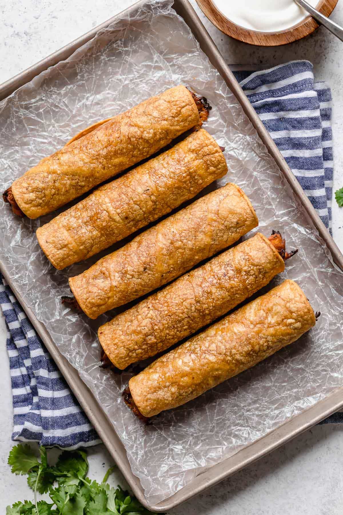 Baked Chicken Taquitos Rolled chicken taquitos on a baking sheet before baking.