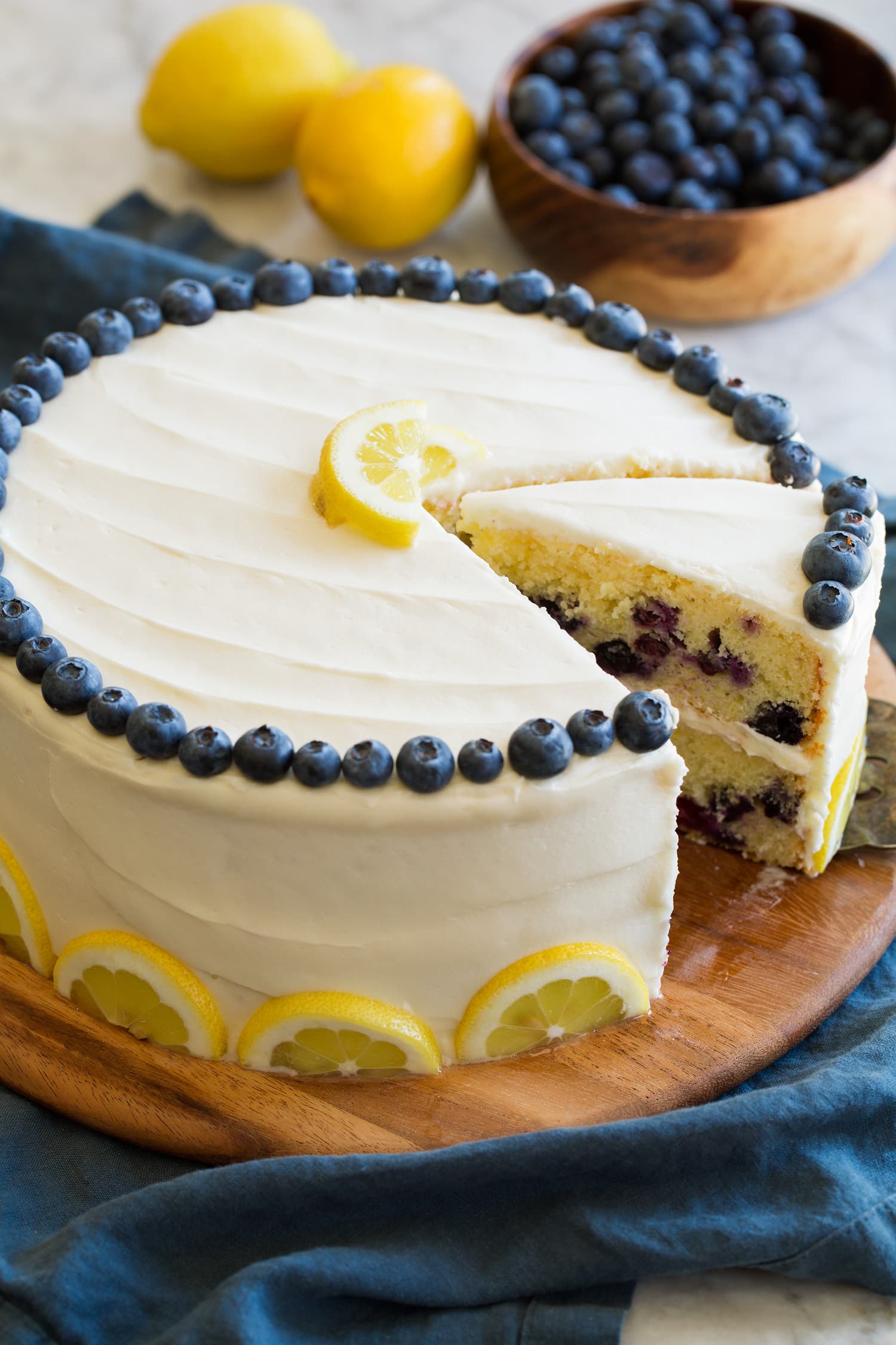 Lemon Blueberry Cake Whole cake with sliced removed. Garnished with fresh blueberries and lemon slices.