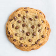 One big chocolate chip cookie shown sitting on white parchment paper.