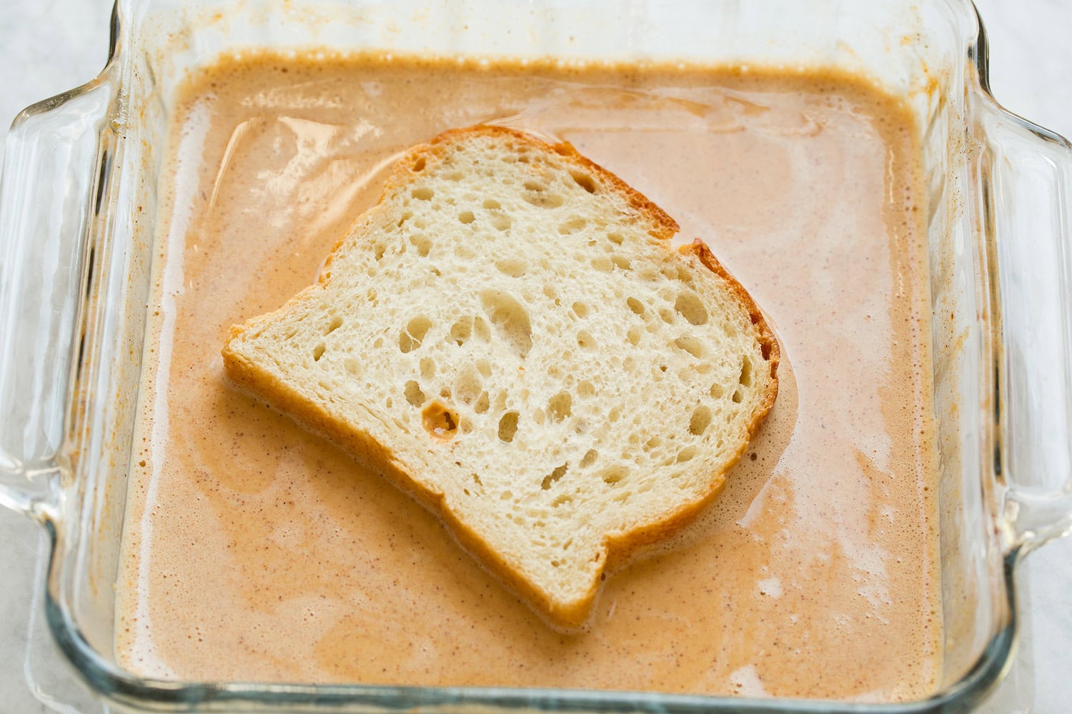 Pumpkin French Toast French bread shown dipped in pumpkin egg custard on first side.