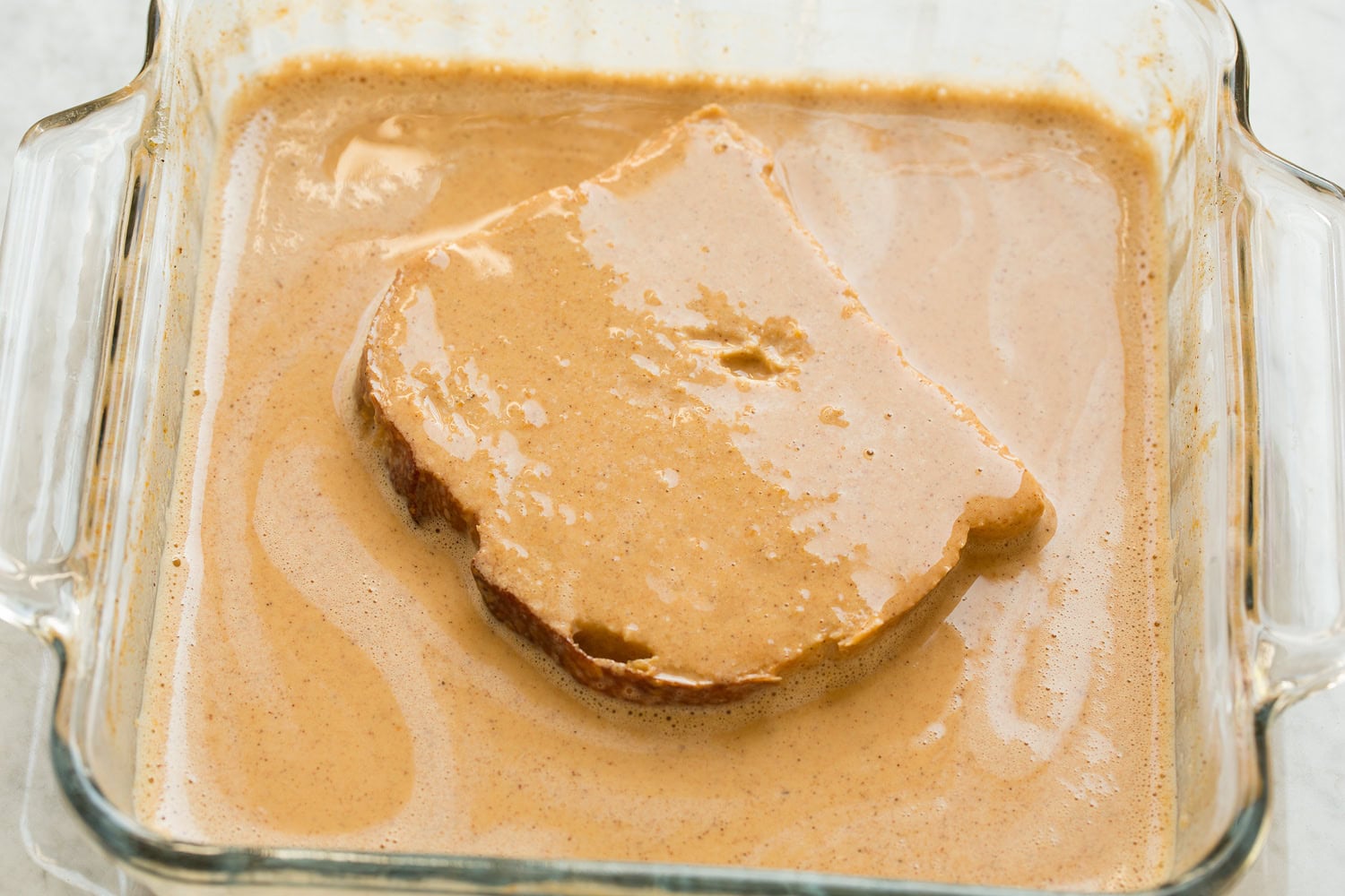 Pumpkin French Toast French bread shown dipped in pumpkin custard mixture on second side.