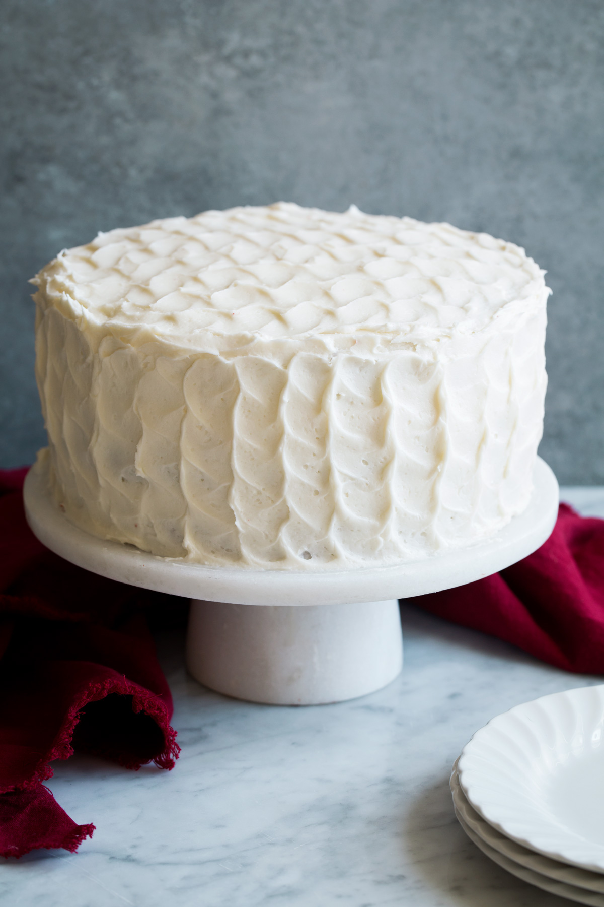 The BEST Red Velvet Cake! Soft, moist and perfectly fluffy! Whole red velvet cake covered in cream cheese frosting with a ruffled design. Cake is sitting on a marble cake stand.