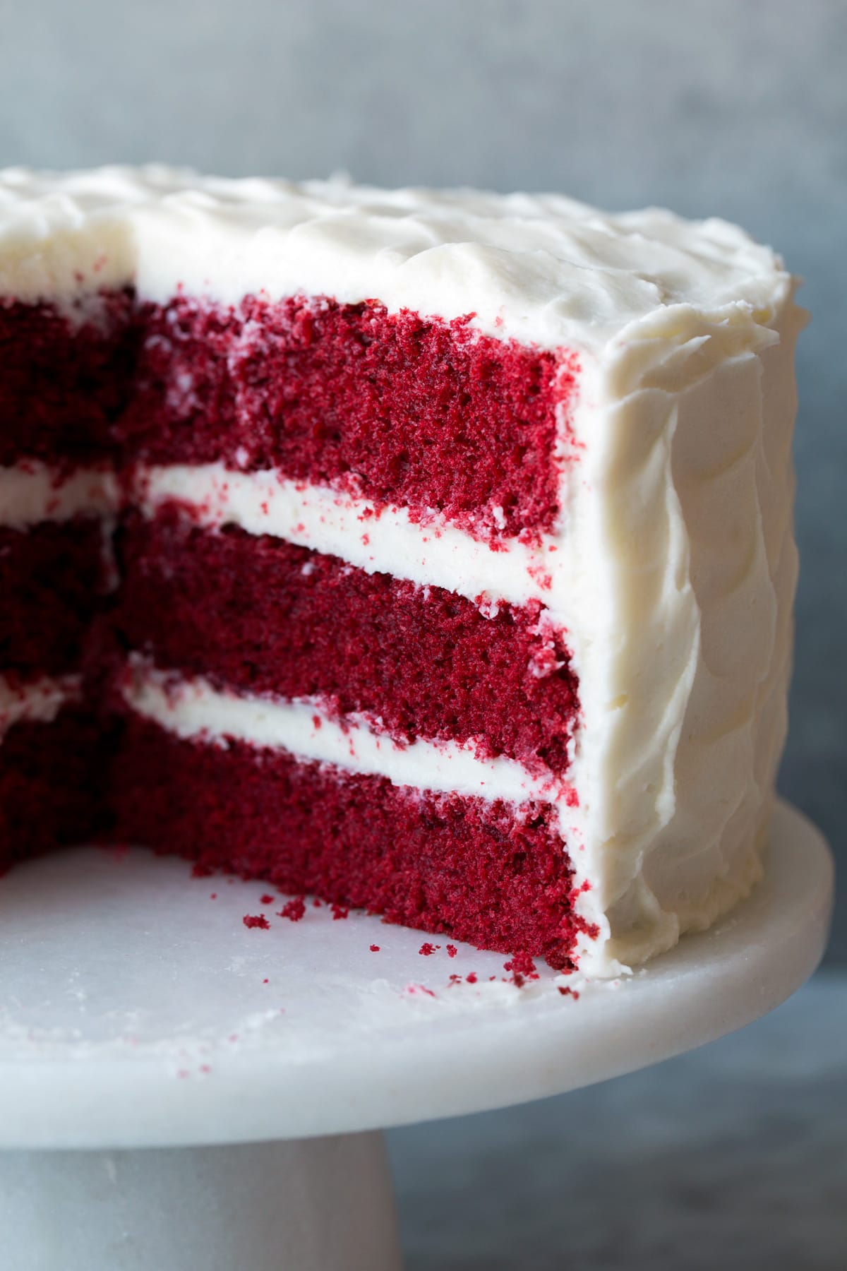 The BEST Red Velvet Cake! Soft, moist and perfectly fluffy! Red Velvet cake with a slice removed to show interior of cake. Cake is resting on a cake stand.