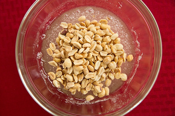 1 cup granulated sugar 1/2 cup light corn syrup 1 cup unsalted peanuts 1/4 tsp salt 1 Tbsp butter 1 tsp vanilla extract 1 tsp baking soda Stirring peanuts into mixture in mixing bowl.