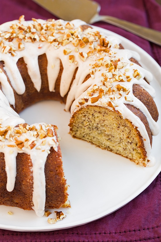 Banana Bundt Cake with cream cheese icing and chopped pecans with slice missing on white plate