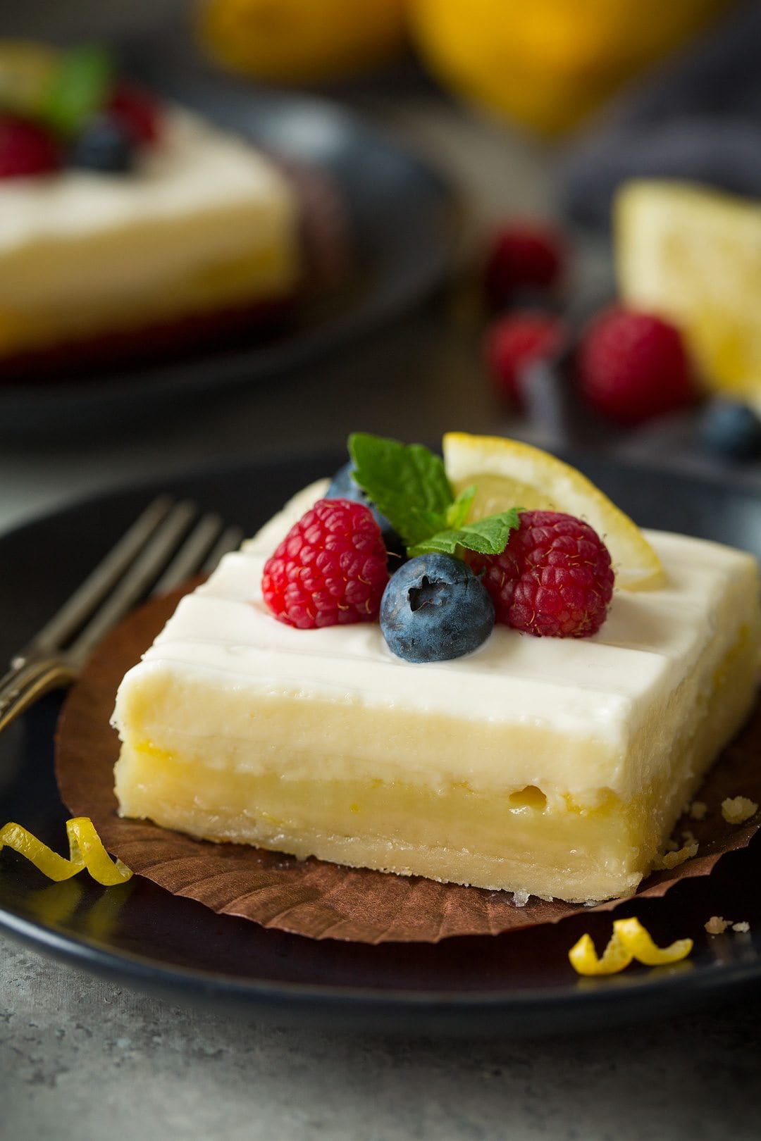 close up of Lemon Cheesecake Bar garnished with berries, lemon, and fresh mint