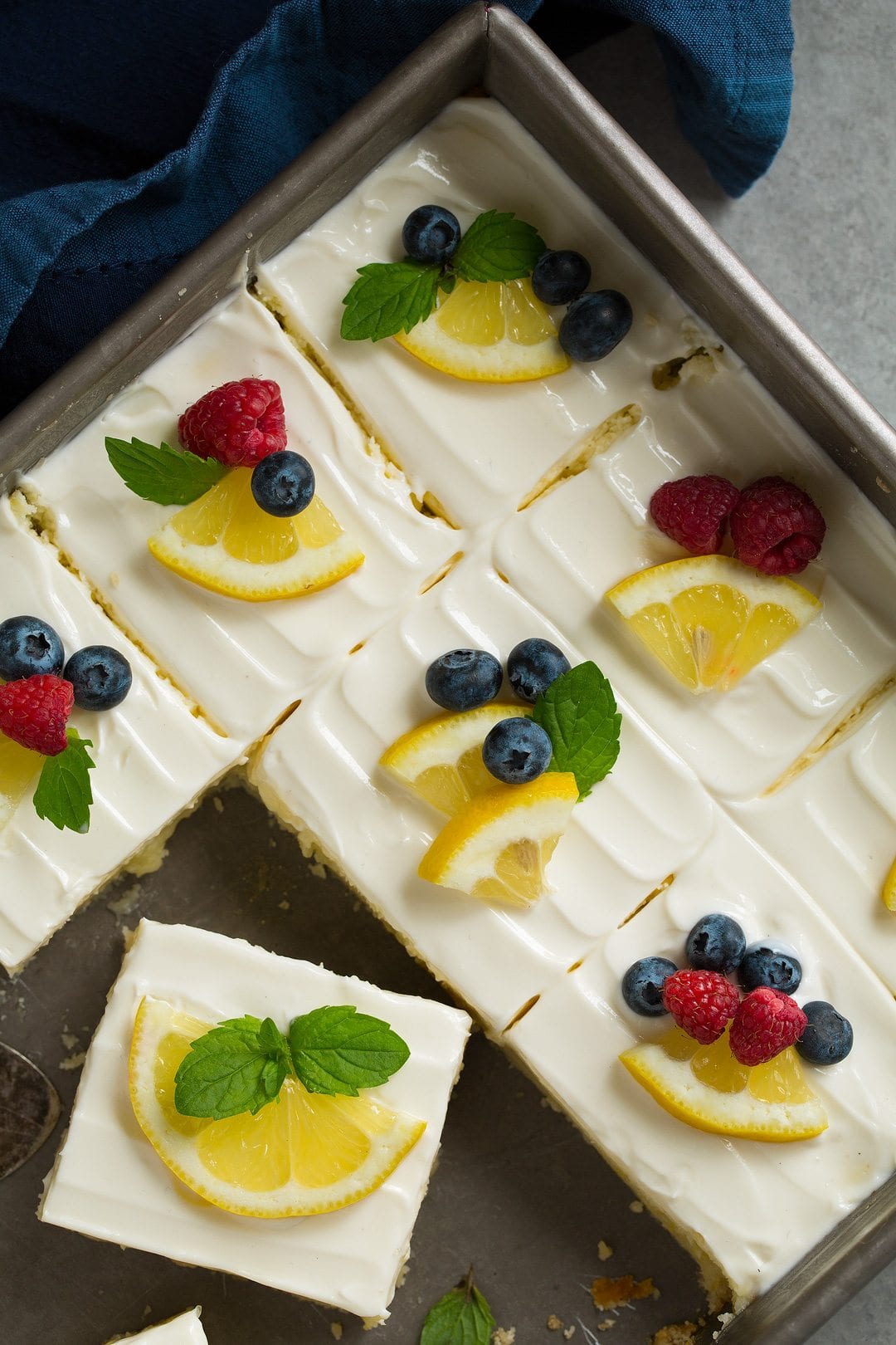 pan of Lemon Cheesecake Bars, sliced and garnished with berries and lemon wedges