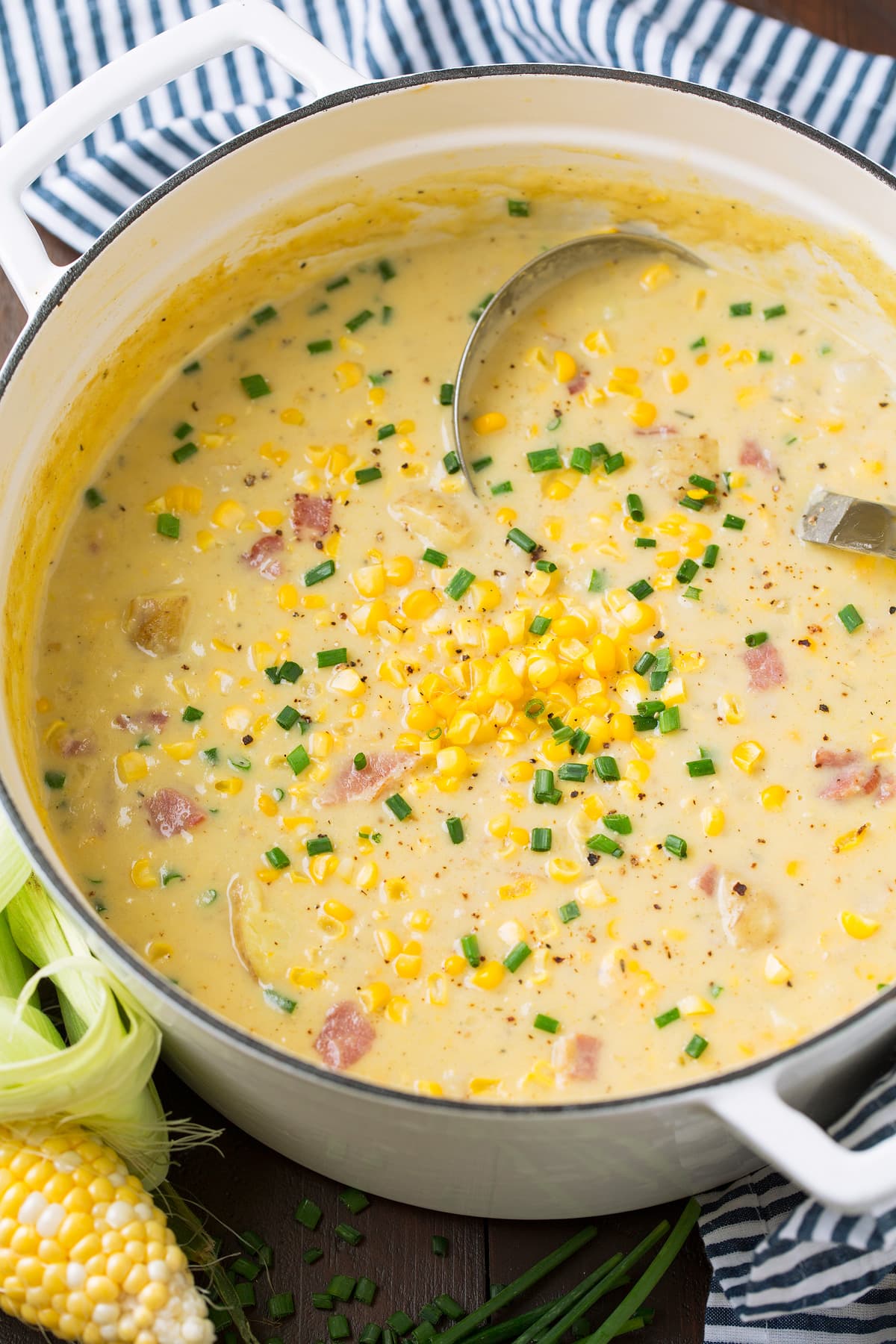 Summer Corn Chowder - a staple summer recipe! Made with an abundance of fresh corn, chunks of tender potatoes and flavorful bacon. All of which is laden in a creamy and rich broth. #cornchowder #soup #vegetablesoup #recipe White enamel pot full of corn chowder soup with a ladle in it.