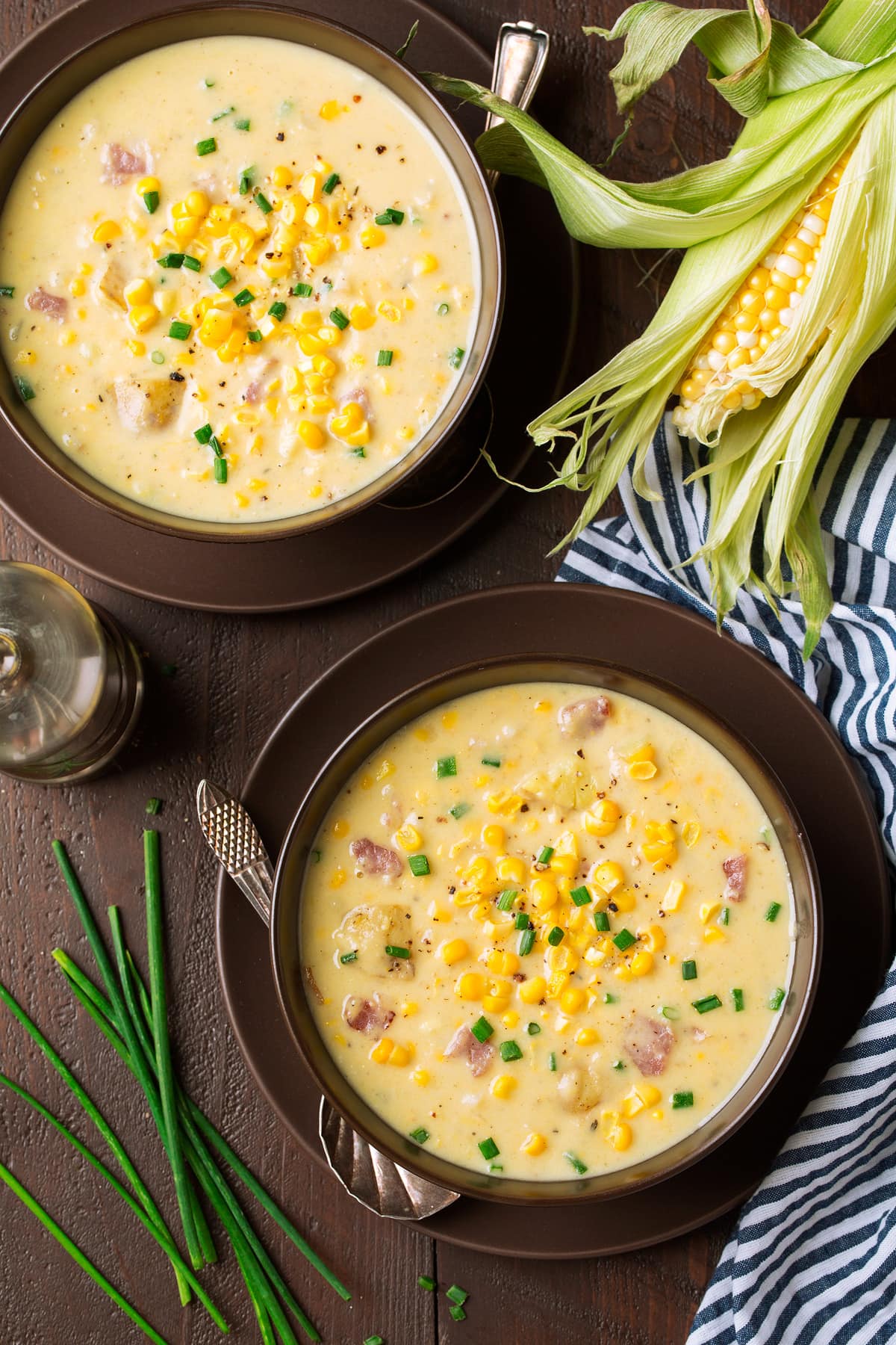 Summer Corn Chowder - a staple summer recipe! Made with an abundance of fresh corn, chunks of tender potatoes and flavorful bacon. All of which is laden in a creamy and rich broth. #cornchowder #soup #vegetablesoup #recipe Two serving of corn chowder in brown serving bowls set on plates.