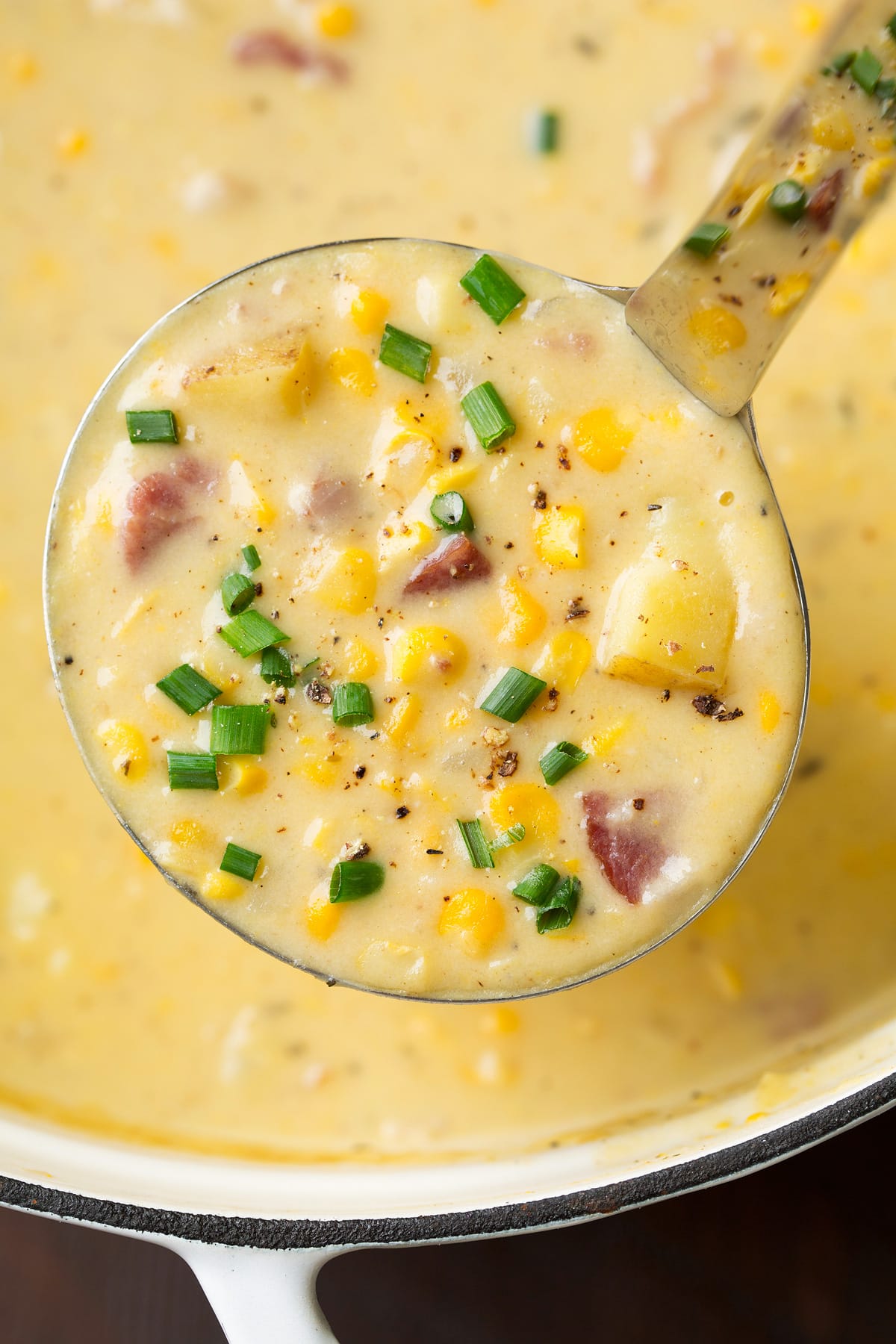 Summer Corn Chowder - a staple summer recipe! Made with an abundance of fresh corn, chunks of tender potatoes and flavorful bacon. All of which is laden in a creamy and rich broth. #cornchowder #soup #vegetablesoup #recipe Close up image of corn chowder with potatoes in a ladle.