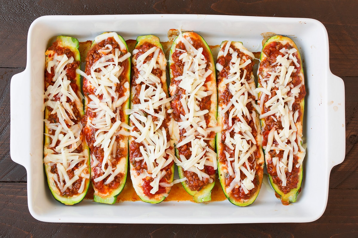 Lasagna Zucchini Boats Adding shredded cheese over sauce layer in zucchini boats.