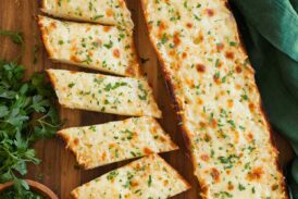 Two halves of cheese garlic bread on a cutting board, one is cut into slices.