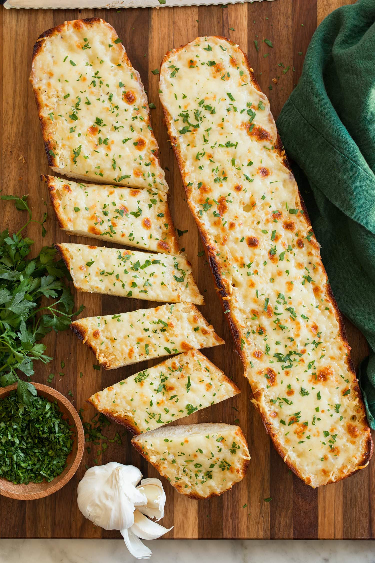 Two halves of cheese garlic bread on a cutting board, one is cut into slices.