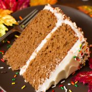Layered spice cake with cream cheese frosting on a matte brown plate decorated with fall colored sprinkles.