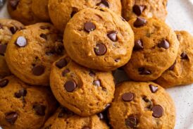 Image of pumpkin chocolate chip cookies stacked on a white serving plate.