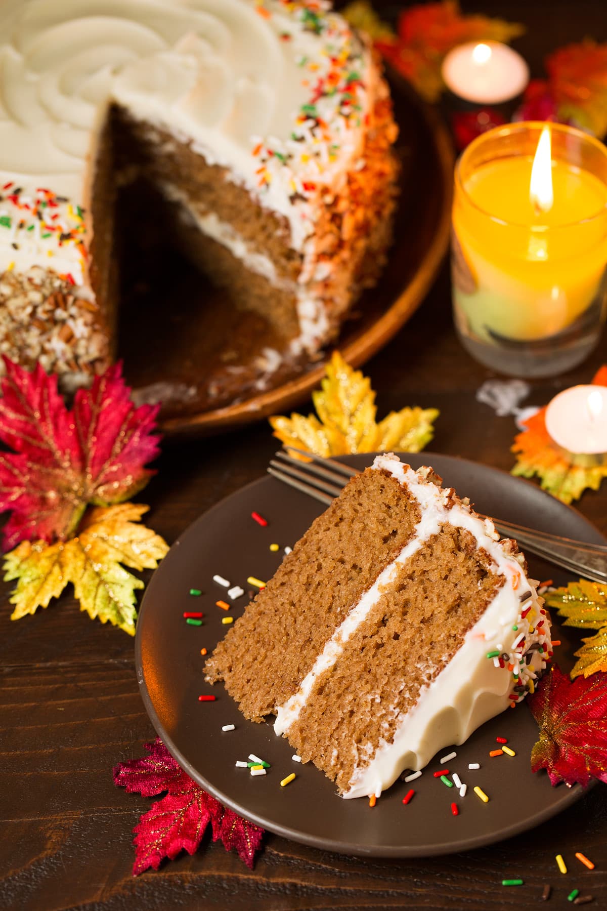 Spice Cake One slice of spice cake on a single serve plate and a whole spice cake is in the background. Decorations in the image include fall leaves, a lit candle and a wooden surface.