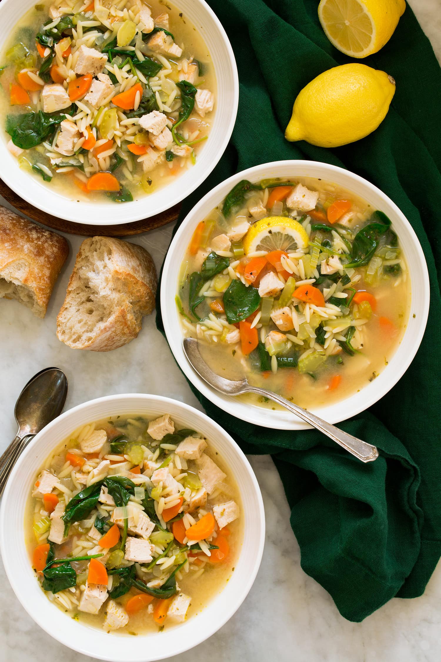 Lemon Chicken Orzo Soup Three bowls of chicken soup with orzo, lemon, spinach, carrots, celery and onions.