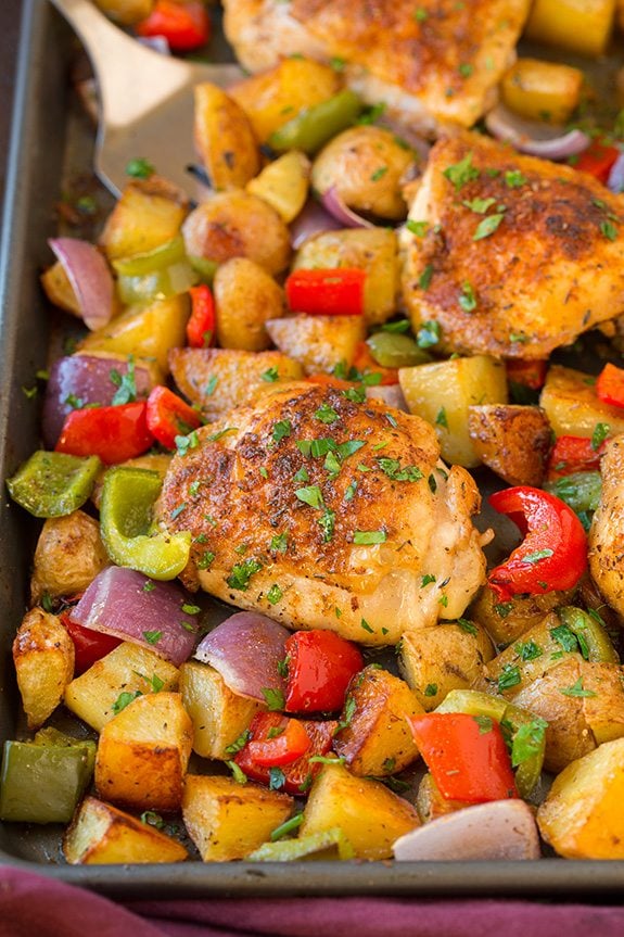 Baked cajun chicken thighs and veggies with cajun seasoning on a sheet pan.