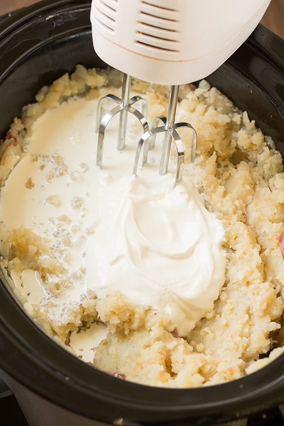 Slow Cooker Garlic Mashed Potatoes Mixing milk and sour cream in to mashed potatoes with an electric hand mixer.