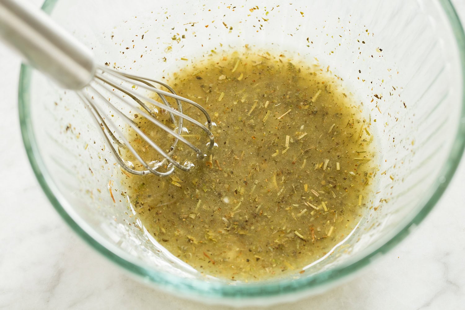 Caprese Chopped Salad Chicken marinade shown in a glass bowl with a whisk, after mixing and blended.