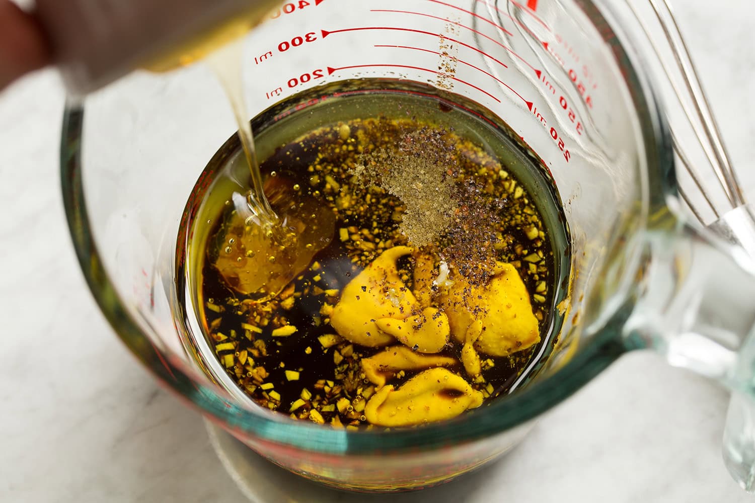 Caprese Chopped Salad Balsamic salad dressing ingredients shown in a glass measuring cup before mixing. Include balsamic vinegar, olive oil, dijon mustard, garlic, honey, salt and pepper.