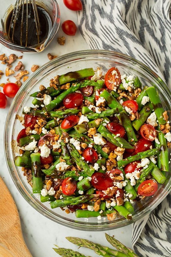 A super delicious asparagus, tomato and feta salad drizzled with an easy balsamic vinaigrette. This salad uses few ingredients but they're all powerful in flavor creating an incredible salad that you won't be able to stop eating! #cookingclassy #asparagus #tomato #feta #salad Asparagus, Tomato and Feta Salad in a glass bowl with Balsamic Vinaigrette at the side